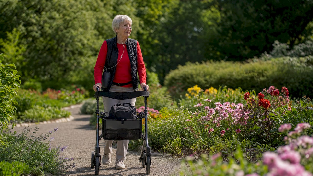Senior woman walking outdoors using portable oxygen and walker