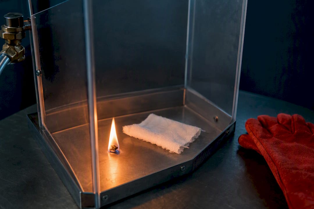 Controlled flame beside fabric in safety chamber